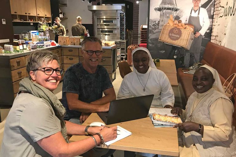 Ronneke Kuiper van Bake for Life en grafisch vormgever Wiep van der Meulen in overleg met de sisters Veronicah en Elisabeth bij gastheer bakkerij By Boonstra in Heerenveen.